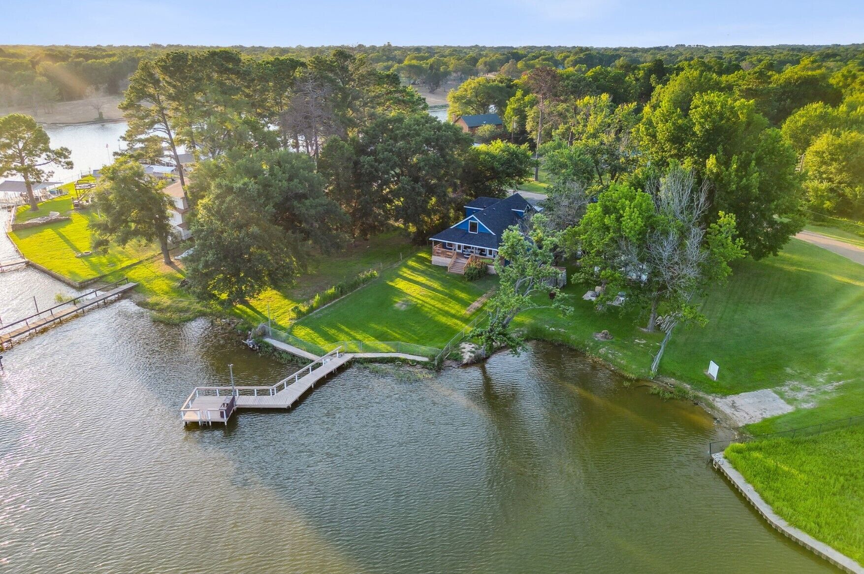 A house with a dock extending into a lake, surrounded by lush greenery and a well-maintained lawn.