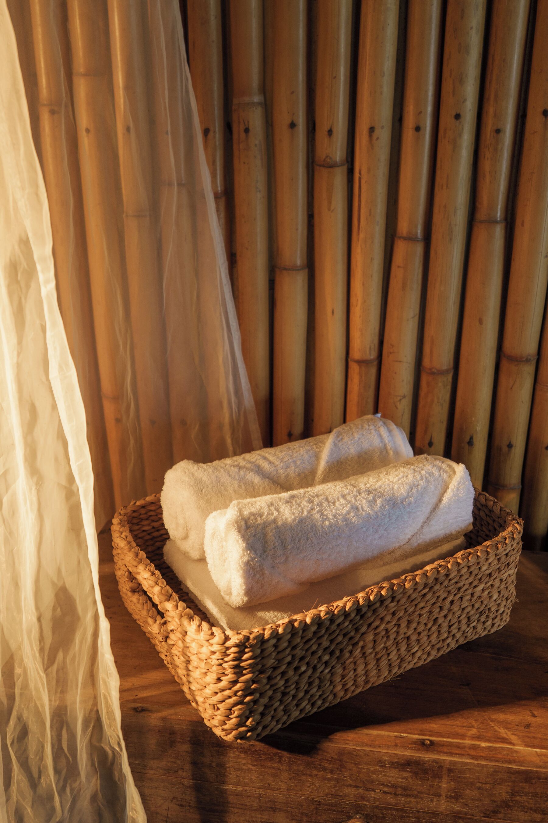 A woven basket containing folded towels on a wooden surface with a bamboo backdrop.