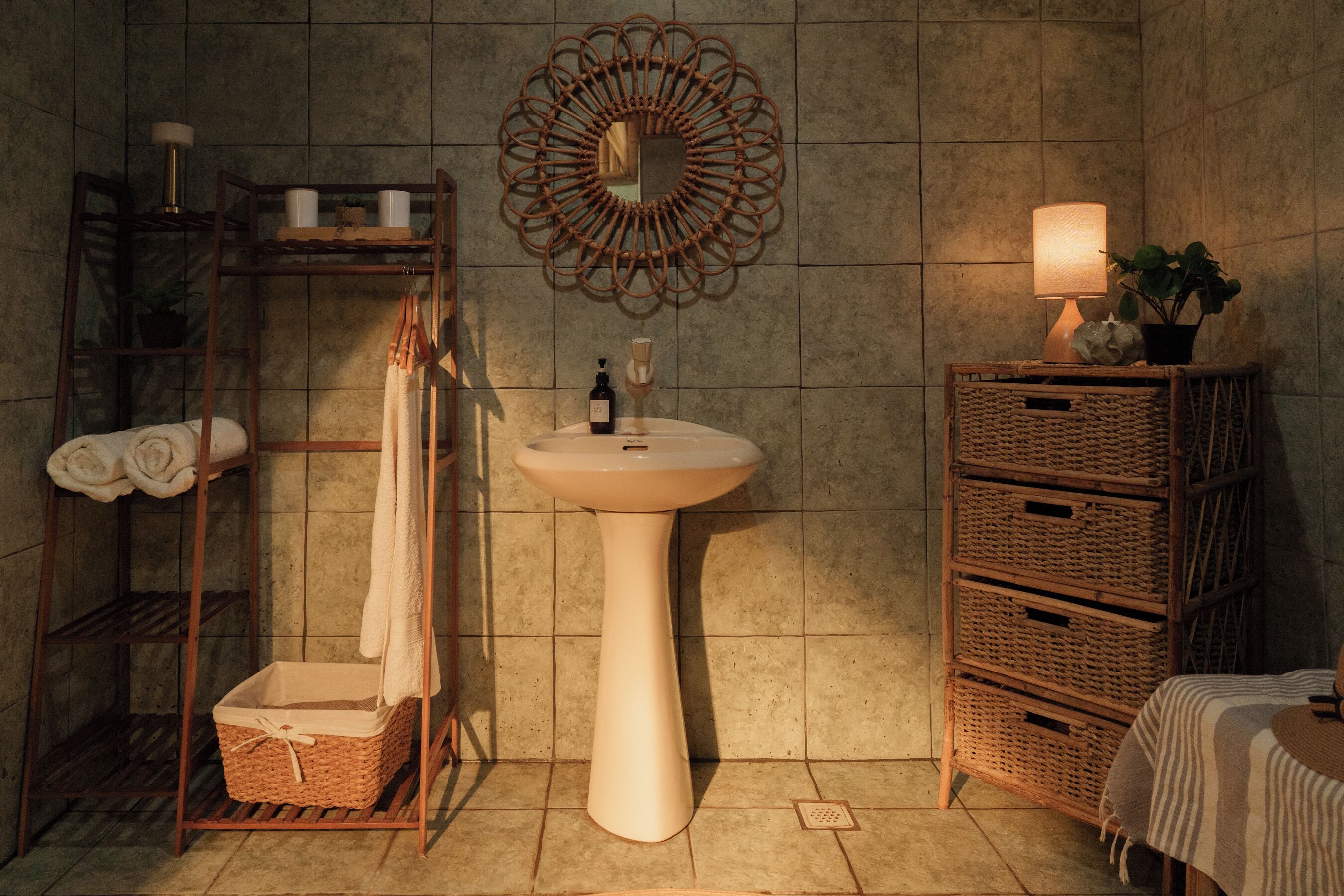 A bathroom with a pedestal sink, a mirror with a decorative frame, a towel rack with towels, and wicker baskets.