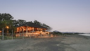 A beachfront property with a thatched-roof building, a fenced area, and a sandy beach. - Serene beach front Villa near Vigan (San Juan)