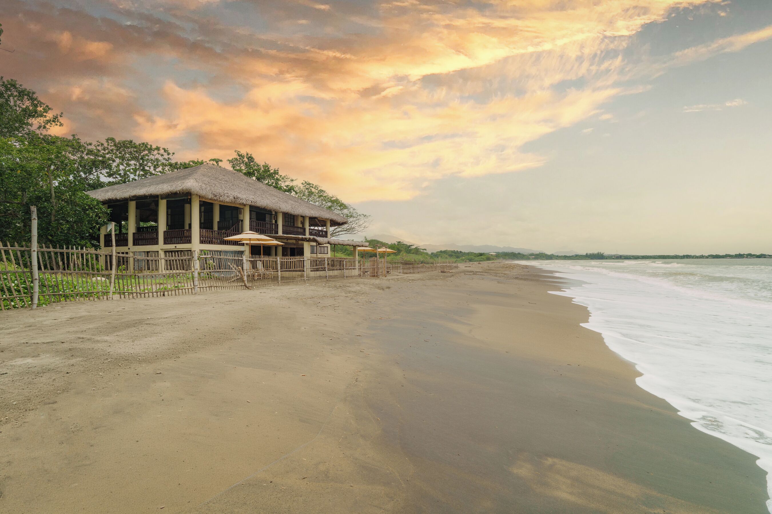 A beachfront property with a thatched-roof building, a sandy beach, and a view of the ocean.