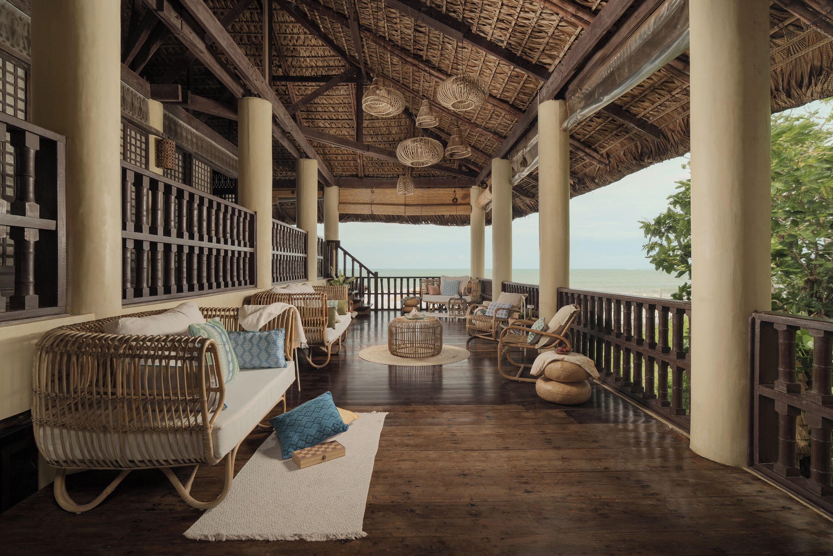 A covered outdoor seating area with wicker furniture, a view of the sea, and a thatched roof.