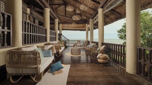 Un espacio de estar techado al aire libre con mobiliario de mimbre, vista al mar y techo de paja.