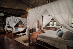 Een kamer met twee bedden, elk met een hemelbed, houten vloeren en uitzicht door een traliewerkraam.