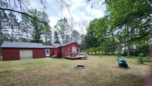 A red single-story house with a garage, a deck, and a fire pit in the yard.