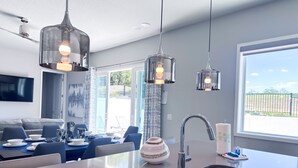 Une cuisine moderne dotée d’un grand îlot central, d’un évier en acier inoxydable et de luminaires suspendus.