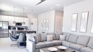Un salon moderne avec un canapé d’angle gris, une table basse et un coin repas comprenant une table et des chaises grises.