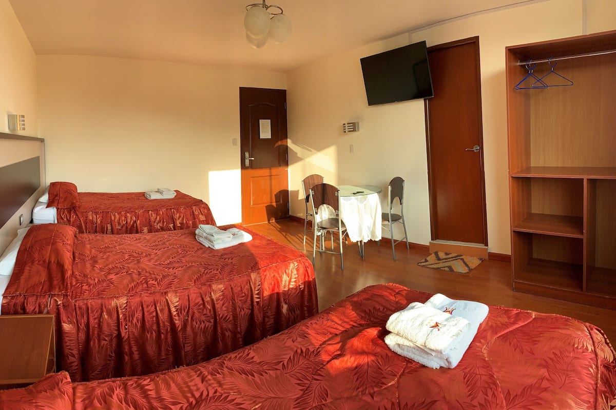 A hotel room with two beds, a desk, a chair, a wardrobe, and a TV.