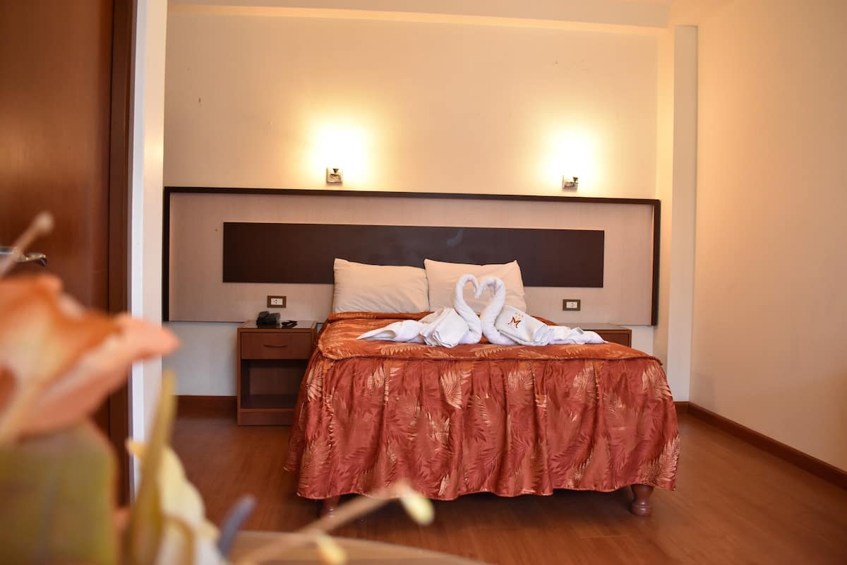 A hotel room with a large bed, a nightstand, and a wall-mounted light fixture.