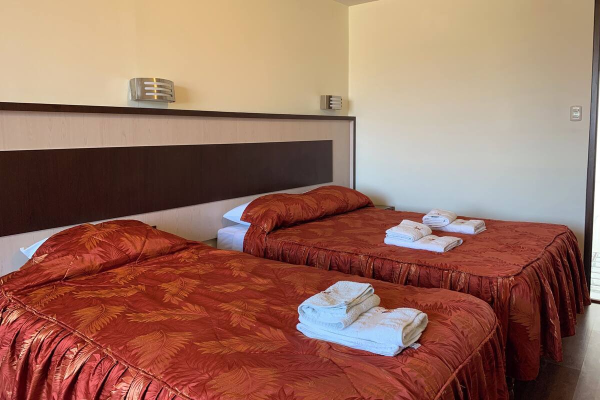 A hotel room with two beds, each with a red patterned bedspread and white towels.