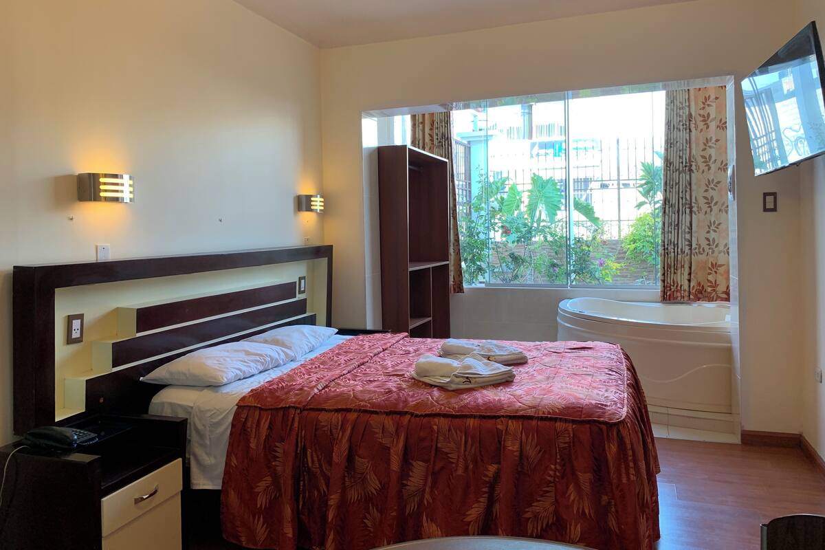 A hotel room with a bed, bedside table, lamp, and a window with curtains.