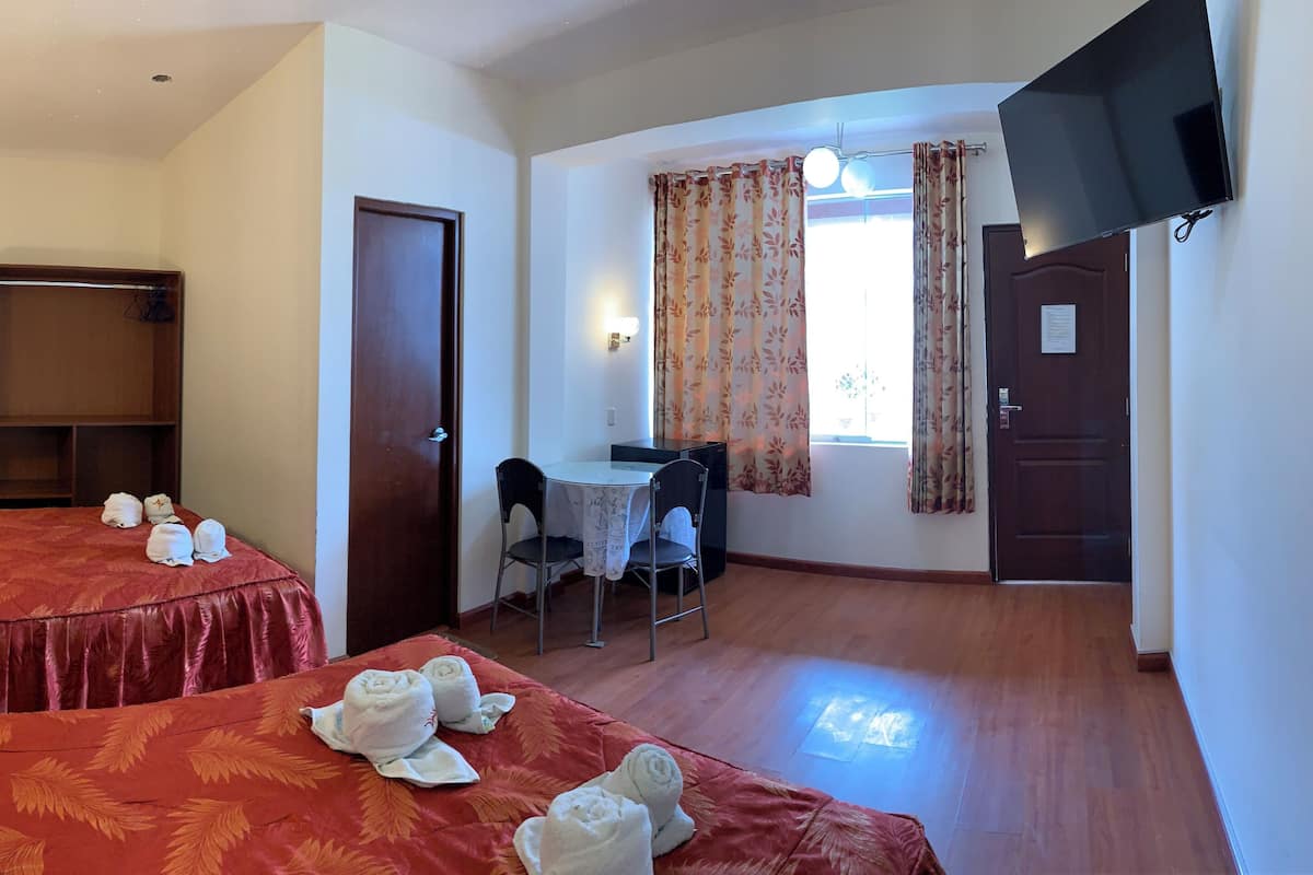 A hotel room with two beds, a desk, a chair, a TV, and a wardrobe.