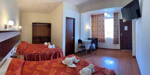 Habitación de hotel con dos camas, un escritorio, una silla, un televisor y un armario.