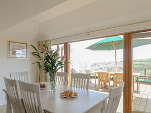 A dining area with a table, chairs, a vase with flowers, and a view of the outdoors.