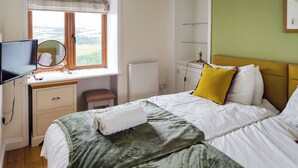 A hotel room with a bed, a desk, a chair, a radiator, and a window with a view.