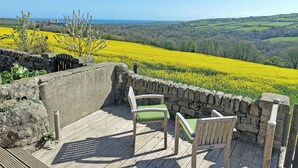 A wooden deck with two chairs overlooking a field of yellow flowers and a distant view of the sea.