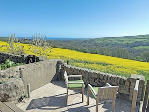 A wooden deck with two chairs overlooking a field of yellow flowers and a distant view of the sea. - 2 bedroom accommodation in Grinkle, near Staithes (Grinkle, near Staithes)