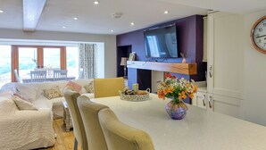 A modern kitchen with a dining area, a TV mounted on the wall, and a clock on the wall.