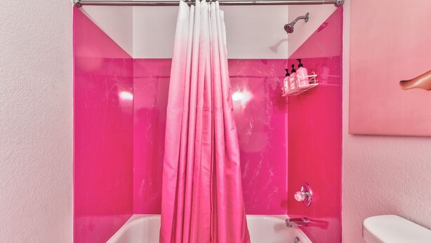 Ein Badezimmer mit einer Duschvorhang in Rosé-Lila-Verlauf, zwei Waschbecken und einer Toilette.
