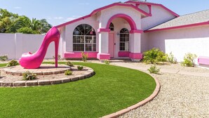 Una casa con fachada rosa, amplios ventanales de arco y una escultura rosa distintiva en el jardín.