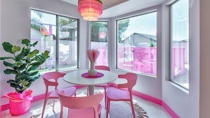Una habitación con una mesa redonda, sillas rosadas, un ventanal grande y una lámpara colgante.