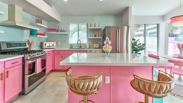 Una cocina moderna con armarios rosa, electrodomésticos de acero inoxidable y una isla central con taburetes de bar.