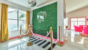 Un vestíbulo de hotel con una pared verde, una bola de discoteca, un espejo con forma de corazón y una decoración rosa y dorada.