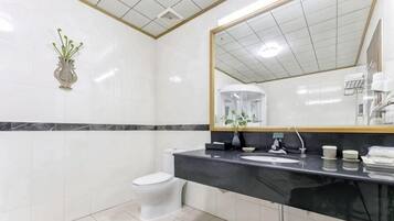 Un baño con inodoro blanco, lavamanos negro, espejo con marco dorado y un florero blanco con plantas verdes en la pared.