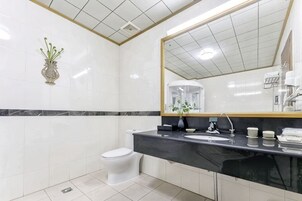 Un baño con inodoro blanco, lavamanos negro, espejo con marco dorado y un florero blanco con plantas verdes en la pared.