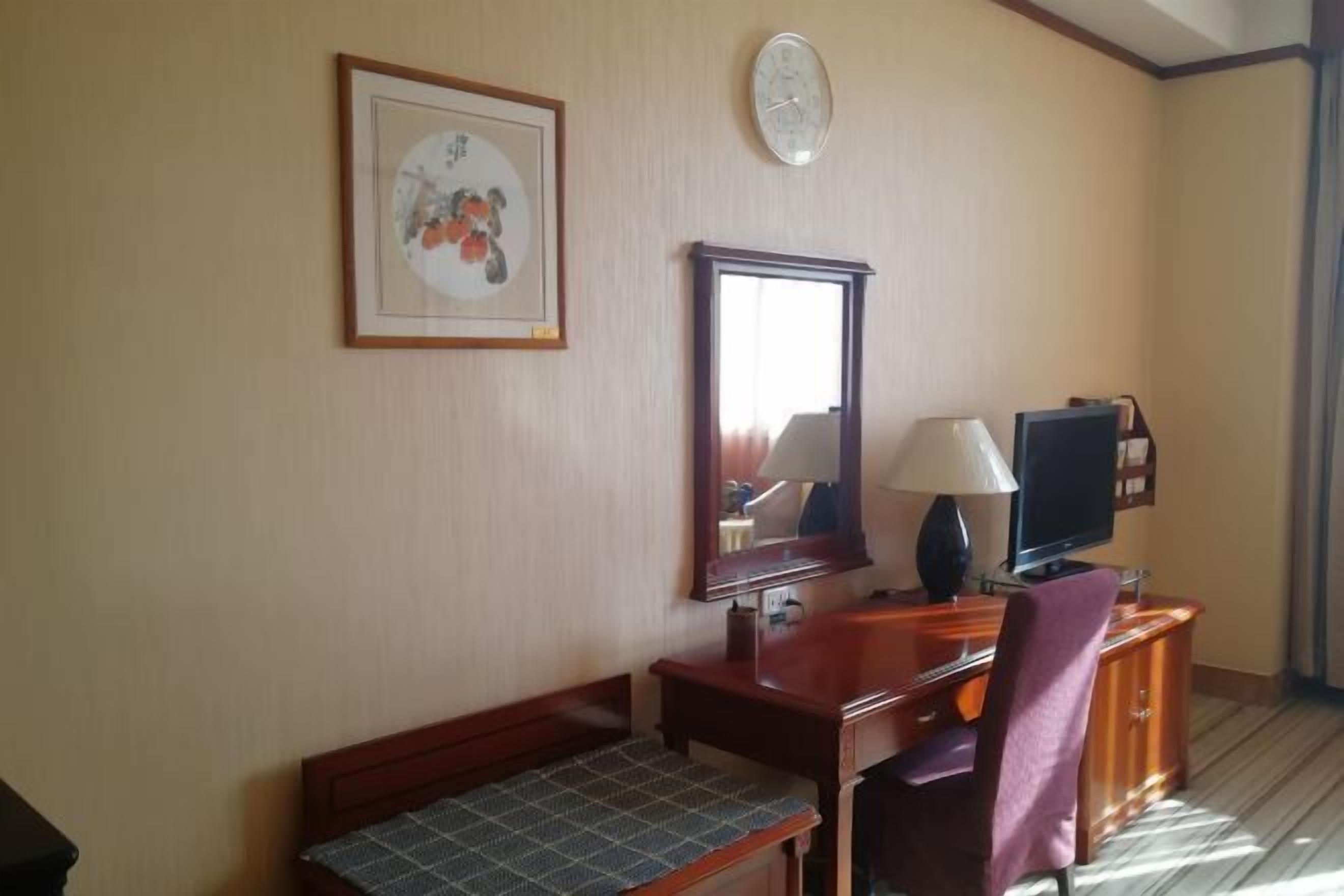 Ett hotellrum med ett skrivbord i trä, en tv, en spegel och en inramad tavla på väggen.