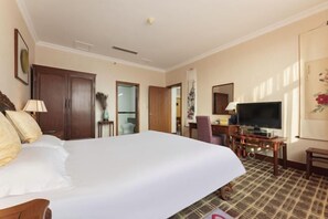 A hotel room with a large bed, a television, a desk, and a chair.