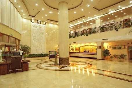 A spacious lobby with a marble column, a reception desk, and a second-floor balcony with plants.. International Academic Exchange Center of Shandong University of Technology Hotel