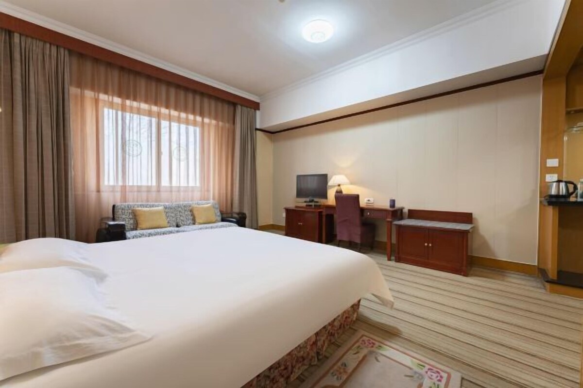 Een hotelkamer met een groot bed, een bureau, een stoel, een televisie en een klein kastje.