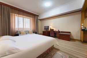Habitación de hotel con una cama grande, un escritorio, una silla, un televisor y un armario pequeño.