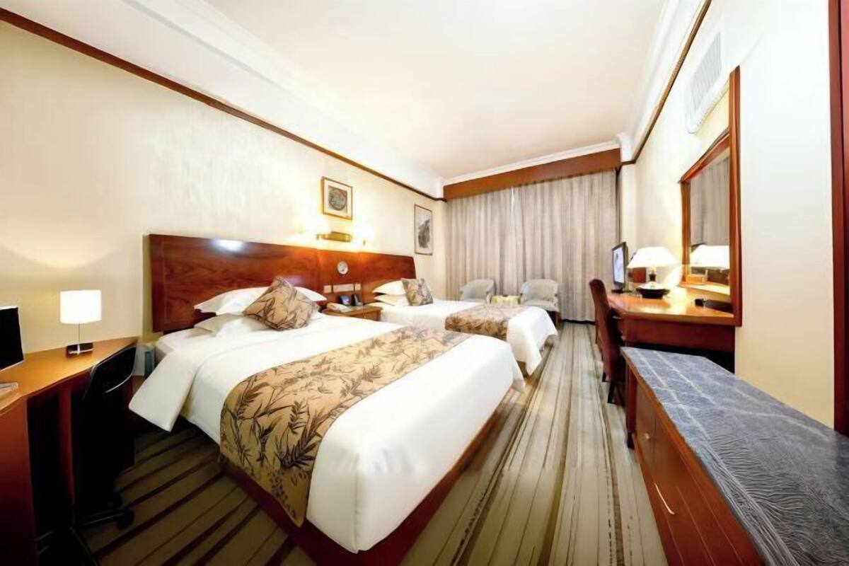 Een hotelkamer met twee bedden, een bureau met stoel, een televisie en een grote spiegel.