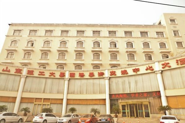 Un immeuble à plusieurs étages doté d’une façade incurvée, de grandes fenêtres et d’une entrée imposante avec une enseigne rouge.