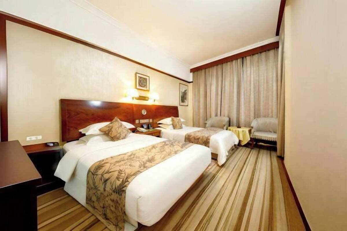 Een hotelkamer met twee bedden, een bureau, een stoel, een klein tafeltje en een raam met gordijnen.