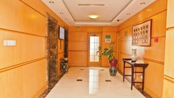 A hotel lobby with a marble floor, wooden paneling, a reception desk, a potted plant, and a framed artwork on the wall.