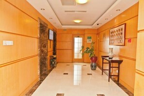A hotel lobby with a marble floor, wooden paneling, a reception desk, a potted plant, and a framed artwork on the wall. - International Academic Exchange Center of Shandong University of Technology Hotel (Zibo)