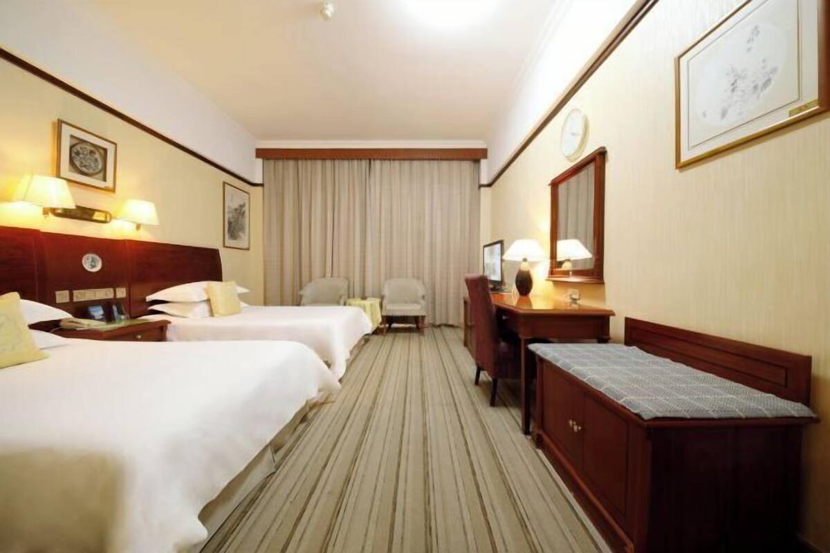 Een hotelkamer met twee bedden, een bureau, een stoel, een dressoir en een groot raam met gordijnen.