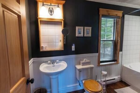 Un baño con lavamanos blanco, inodoro de madera y ventana con persianas.