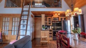 A spacious loft-style room with a wooden ceiling, a loft bed, a dining area with a table and chairs, and a kitchen area with modern appliances. - Charlevoix -  Chalet Le Cormier (Saint-Aimé-des-Lacs)
