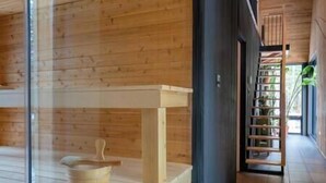 A wooden interior with a glass partition, a wooden bench, and a staircase leading to a balcony.