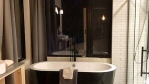 A modern bathroom with a freestanding bathtub, a large mirror, and a view of the outside.