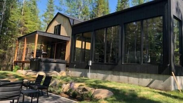 A modern house with large windows and a deck, surrounded by trees.