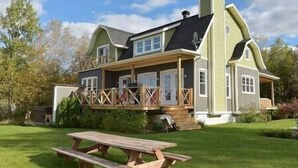 Una casa de dos pisos con un porche, una chimenea y una mesa de picnic en el jardín delantero.