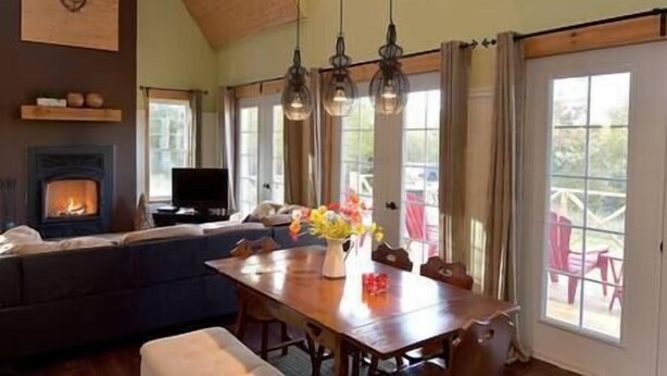 Una sala de estar acogedora con chimenea, una mesa de comedor con sillas y un ventanal con cortinas.