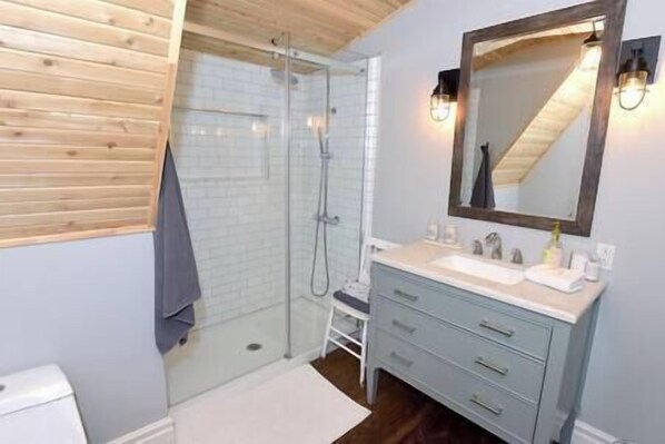 A bathroom with a glass shower enclosure, a white sink with a mirror, and wooden ceiling beams.