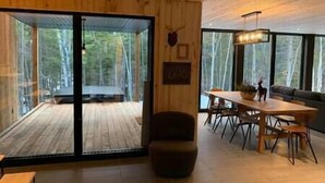 Un intérieur moderne avec un plafond en bois, un coin repas comprenant une table et des chaises, un canapé et une grande porte-fenêtre coulissante donnant sur une terrasse extérieure.
