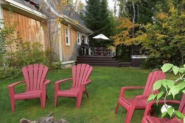 A backyard with a wooden deck, a grill, and three red Adirondack chairs.